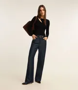 Blusa negra de punto acanalado, con mangas largas, cuello redondo con detalle metálico dorado y abertura asimétrica en el hombro.