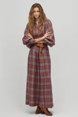 Camisa larga de lino a cuadros color avellana, con cuello camisero clásico, mangas largas abullonadas con puños elásticos, botones de nácar frontales y ruedo curvo, un poco más largo atrás. Incluye cinturón de cuero marrón.