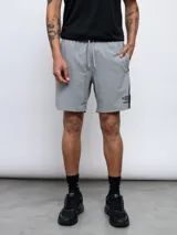 Short deportivo gris de entrenamiento, con cordón ajustable en la cintura, logo de la marca en la pierna izquierda y detalle de línea vertical negra en el lateral.