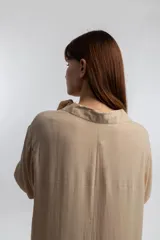 Vestido camisero midi color beige, de corte holgado, con cuello camisero, mangas largas con puños abotonados y aberturas laterales en el ruedo.