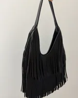 Bolso de hombro negro con diseño de flecos largos que cubren la mayor parte del cuerpo del bolso. Tiene un asa corta y curva.