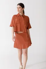 Camisa corta de manga corta color rojo, con doble cartera diagonal con botones de madera, cuello clásico y botamangas marcados. Tiene un bolsillo con aplique de crochet hecho a mano con forma de frutilla.