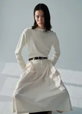 Jersey color crudo de punto fino con cuello perkins, manga larga y detalle de botones metálicos en el hombro. Corte recto.