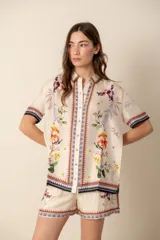 Camisa de seda color crema con estampado floral y de aves, de corte recto, manga corta y cuello camisero.