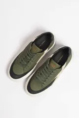 Zapatillas deportivas color verde militar con detalles en negro y beige. Presentan cordones negros, suela blanca y un rayo beige en el lateral.