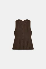Top de punto acanalado en color beige, sin mangas y con cuello redondo. Presenta un cierre frontal con botones pequeños y un bajo con acabado en peplum que aporta volumen.