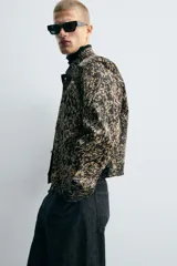 Cazadora corta (cropped fit) de piel con acabado de pelo, estampado abstracto en tonos negro y beige/tostado. Presenta cuello solapa, manga larga y cierre frontal con botones metálicos.