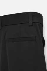 Pantalón negro de corte ancho con cinturón de tela con hebilla metálica y pliegues frontales.