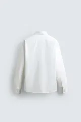 Camisa celeste de algodón con estructura twill, corte regular, cuello solapa, manga larga con puños abotonados y cierre frontal con botones.