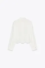 Camisa blanca corta de cuello solapa y manga larga. Bajo con bordados perforados combinados a tono. Cierre frontal con botones.