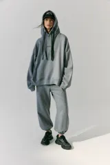 Buzo gris de frisa con capucha, bolsillos delanteros y corte oversize. Tiene recortes laterales, doble cordón con puntera de goma y estampa en frente y espalda.