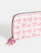 Billetera pequeña de cuerina color blanco con estampado de lazos rosas y corazones. Tiene cierre circundante y tirador de goma.