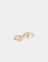 Set de tres anillos dorados de metal con diferentes diseños: uno con un corazón rosa, otro con forma de rosa y otro con una perla sintética.