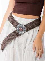 Cinto marrón trenzado con hebilla circular plateada con piedra marrón al centro.