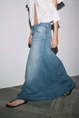 Falda larga de denim azul, de tiro alto, con trabillas y cinco bolsillos. Cierre frontal con cremallera y botón metálico.