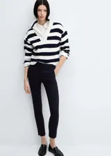 Pantalón negro de corte skinny y largo cropped, confeccionado en tejido fluido con forro interior. Presenta tiro medio, trabillas, bolsillos laterales y traseros de ribete. Cierre frontal con cremallera y botón.