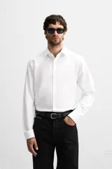 Camisa blanca de corte slim fit, confeccionada en algodón, con cuello italiano, mangas largas con puños abotonados y cierre frontal con botones.