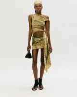 Conjunto de top y falda corta con estampado abstracto en tonos beige y verde. El top es de un solo hombro con abertura en el abdomen y la falda es cruzada con lazo lateral.