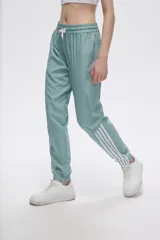 Pantalón de jogging color celeste con cintura elástica ajustable con cordón y puños elásticos. Presenta tres tiras verticales blancas en la parte inferior de la pierna.
