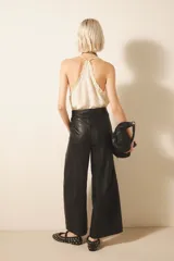 Pantalón ancho de cuero ovino color negro, con pinzas delanteras, cierre con snaps metálicos y tiras ajustables en la cintura.