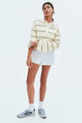 Remera polo de manga larga con rayas horizontales en tonos blanco, amarillo y negro. Tiene cuello clásico y tapeta con botones.