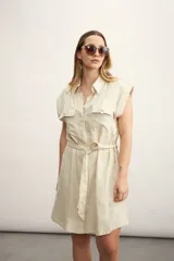 Vestido camisero corto color beige, con cuello clásico, mangas cortas con puños, dos bolsillos con solapa en el pecho, cinturón de lazo y cierre frontal con botones.