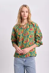 Blusa de manga larga con estampado floral en tonos mostaza, verde y rosa. Tiene cuello redondo con lazo ajustable.