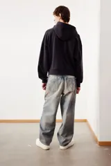 Campera con capucha en felpa de algodón pesado, color negro, con cierre y bolsillos delanteros, hombros caídos y corte oversized.