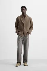 Camisa color arena de lino con cuello abotonado, manga larga con puños abotonados, corte regular y bajo con aberturas laterales.