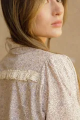 Camisa de algodón con estampado floral, cuello clásico, cierre frontal con botones, mangas largas con puños fruncidos y detalle de puntilla en puños y espalda.