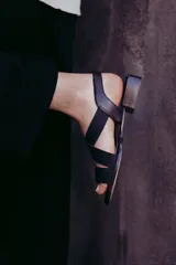 Sandalias bajas color beige con tiras cruzadas y elástico dorado en el talón.