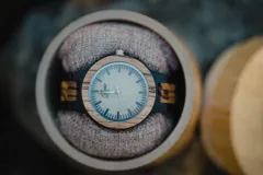 Reloj de pulsera con caja y esfera de madera clara, malla de madera oscura con incrustaciones de madera clara.