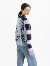 Cardigan oversize de punto jacquard multicolor con predominancia de celeste y azul marino. Cuenta con cuello en V, cierre frontal de botones y un diseño artístico que incluye bordados de cerezas y flores. Las mangas largas presentan un patrón de franjas horizontales.