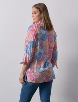 Camisa estampada con hojas en tonos celeste, naranja y verde. Tiene cuello con solapa, abertura central con botones, bolsillos aplicados en la parte delantera y mangas 3/4 con lazo.