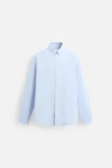 Camisa celeste de algodón, corte relaxed fit, cuello abotonado, manga larga con puños abotonados y cierre frontal con botones.