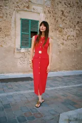 Vestido midi color crema, de cuello redondo y sin mangas. Presenta falsos botones frontales, cinturón elástico con aplique dorado, bolsillos de parche con solapa y abertura delantera.