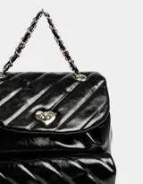 Mochila negra de cuerina acolchada con diseño de líneas diagonales. Tiene solapa con broche decorativo y botón para cerrar. Cuenta con correas regulables, manija superior de material principal y metal, y tira de ajuste de metal.