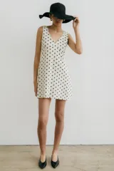 Vestido corto color crema con estampado de lunares negros, escote en V y sin mangas.