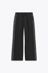 Pantalón de tiro alto negro a rayas verticales blancas, con cintura elástica ajustable con cordones, bolsillos delanteros y banda lateral blanca.