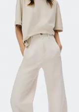 Pantalón de mezclilla color beige claro, de tiro alto y corte ancho (wide leg) que cae recto y amplio hasta el suelo. Presenta cierre frontal y bolsillos laterales.