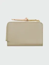 Billetera Marc Jacobs modelo The Utility Snapshot Slim Bifold, de cuero color beige con aplique frontal en cuero color crema y logo dorado. Tiene cierre perimetral con tirador de cuero rosa.