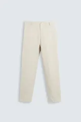Pantalón de vestir color beige confeccionado en lino, de corte recto, con bolsillos laterales y traseros. Se ajusta a la cintura con cinturón de cuero marrón.