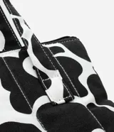 Funda para notebook con diseño tipo cartera, confeccionada en algodón con estampado floral bicolor en blanco y negro. Tiene cierre de cremallera y asa mediana.