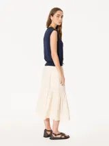 Pollera midi color verde grisáceo, confeccionada en poplín liviano. Presenta cintura elastizada con cordón ajustable, bolsillos tipo plaque con fuelle y tapa, y un recorte con volado fruncido en el ruedo.