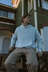 Buzo con capucha celeste, de manga larga y fit loose. Confeccionado en tejido loop back cepillado por dentro, con mangas ranglán, puños de canalé, forro de la misma tela en el interior de la capucha y estampa en goma de tacto suave ubicada en la espalda.