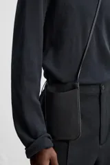 Bolso bandolera negro de cuero con bolsillo plano frontal y correa fina al hombro.