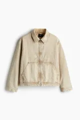 Campera color beige de sarga de algodón con efecto lavado, corte holgado, cuello clásico, cierre frontal con cremallera, bolsillos delanteros de parche, bolsillo interior con botón a presión, botones a presión ajustables en los puños y en los laterales del bajo y forro interior.
