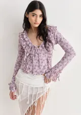 Top de manga larga color celeste/turquesa, confeccionado en tejido de encaje floral. Presenta escote en V con volados en el borde y lazos ajustables en el centro del escote y en los puños.