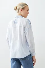 Camisa fucsia de manga larga con cuello camisero y cierre frontal con botones. Presenta apliques de estrellas bordadas en el frente y en el cuello.