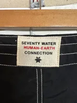 Short de baño negro de largo medio (18 pulgadas) con costuras reforzadas en hilo blanco contrastante. Presenta cordón de ajuste en la cintura y un pequeño logo estampado en la pierna derecha.